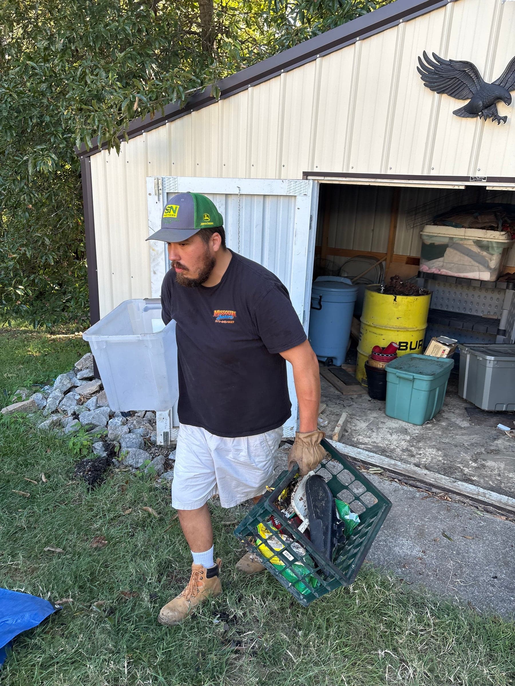 Cole carrying a crate of scrap out of a metal shed's doorway