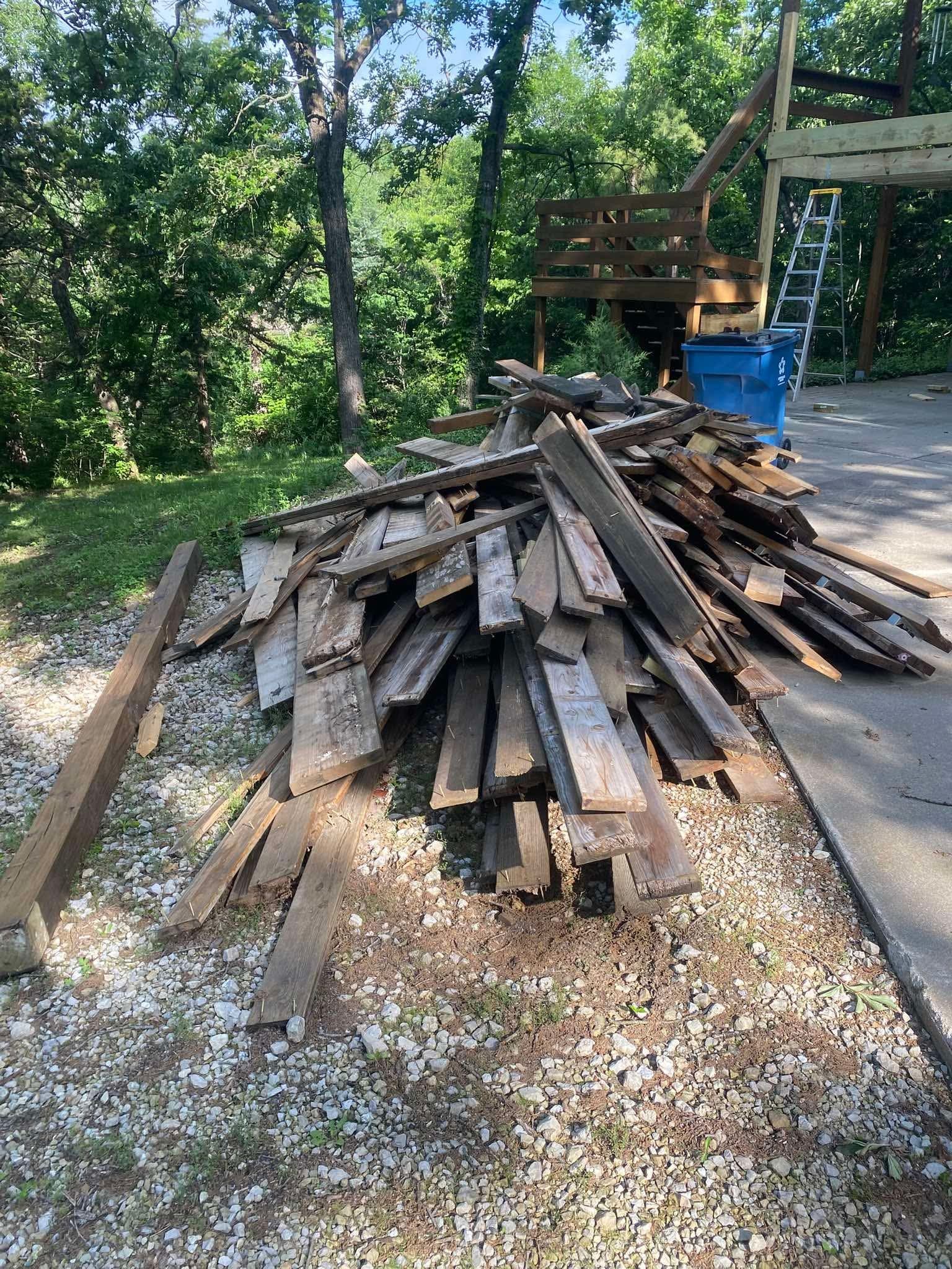 A pile of torn-out deck boards and joists on gravel, the deck frame behind