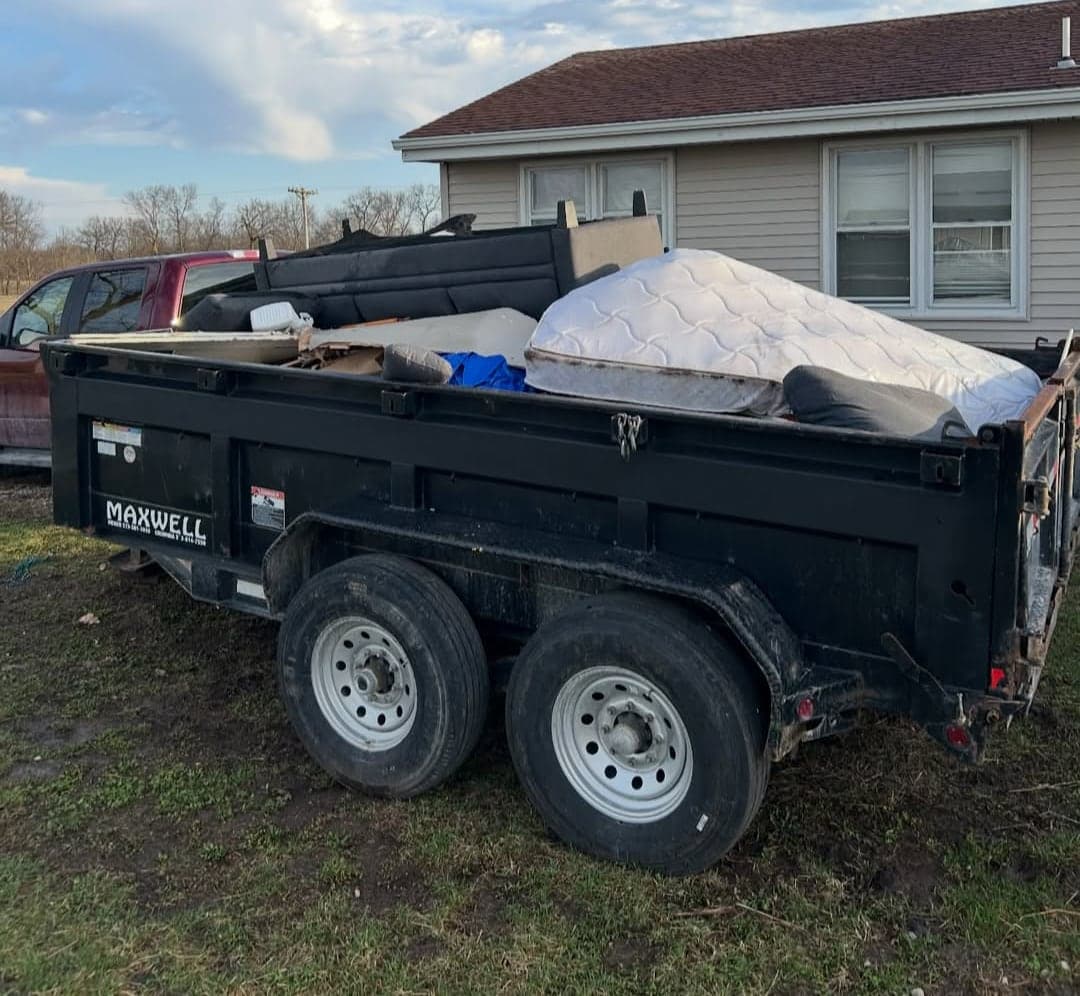Dump trailer loaded with mattresses and furniture next to a house