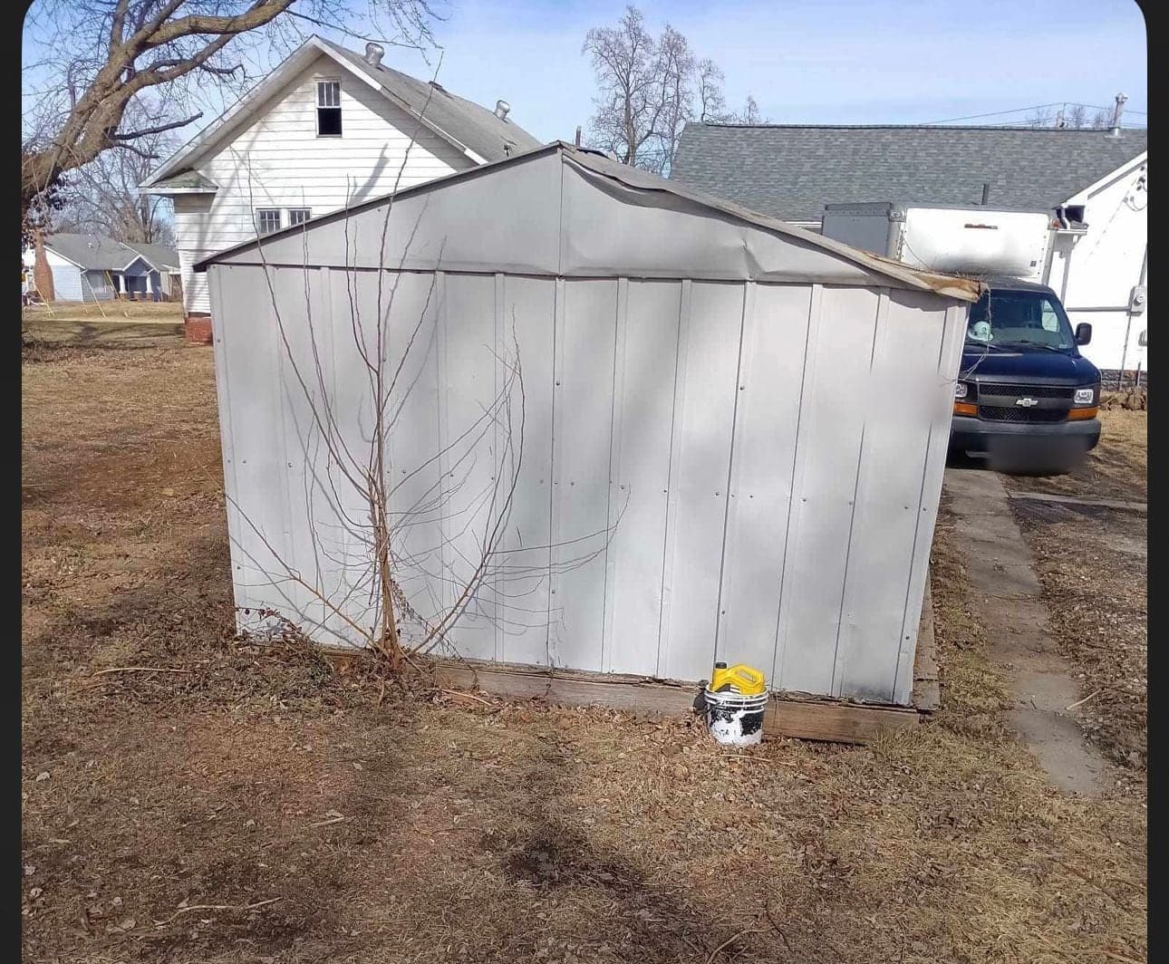 A white metal shed standing in a yard before demolition